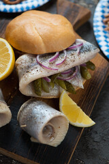 Close-up of german fish sandwich with herring fillet, red onion, pickles, lemon and white bun, selective focus, vertical shot