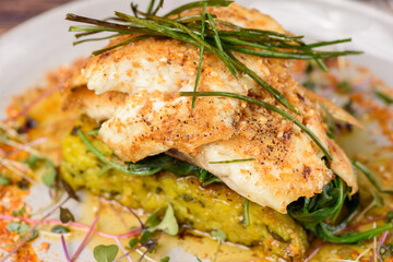 A serve of grilled Barramundi fish with Paella Risotto cake, presented on a round plate
