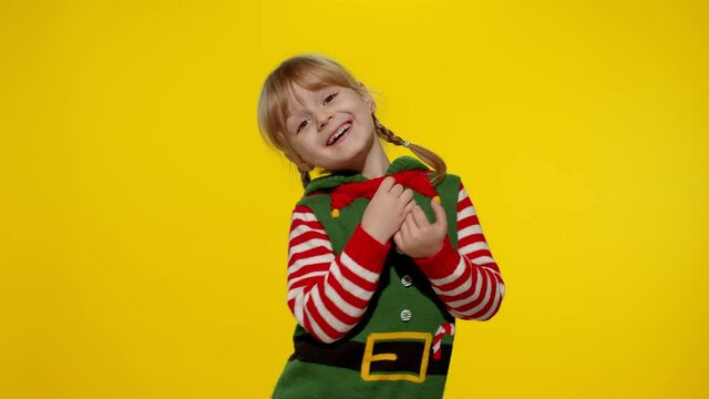 Christmas wish concept. Little fun blonde kid teen teenager girl 5-6 years old in Christmas elf Santa helper costume hopes for dreams come, making a wish, prays for better life. Shy smiling child