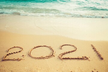 Happy New Year 2021 concept, 2021 number lettering on the sea beach, wave and golden light of sunset.