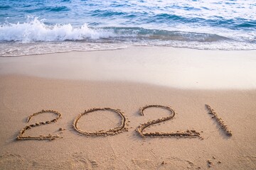 Happy New Year 2021 concept, 2021 number lettering on the sea beach, wave and golden light of sunset.
