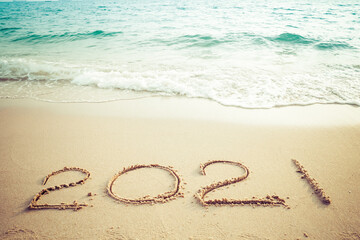 Happy New Year 2021 concept, 2021 number lettering on the sea beach, wave and golden light of sunset.