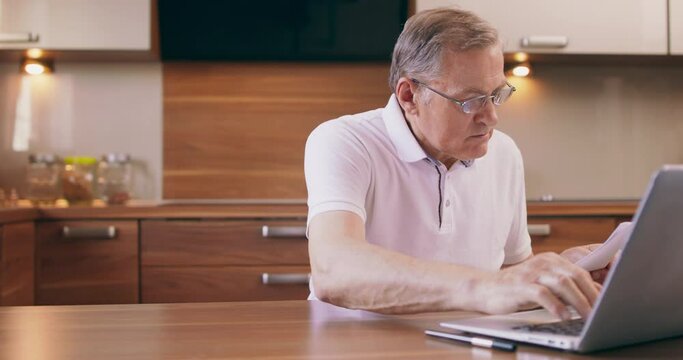 Warm toned portrait of elderly man shopping online or paying taxes holding credit card while using laptop at home, copy space