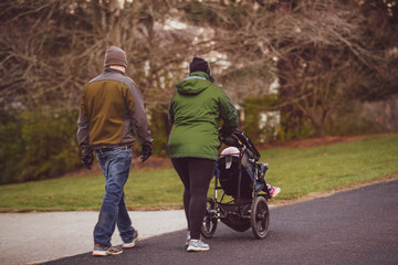 Fototapeta premium Young couple taking a walk with their baby in a stroller in Midwestern neighborhood in winter