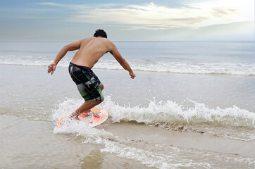 Selective focus, A young asian man is learning to ride skim board. He is turning his body to handle...