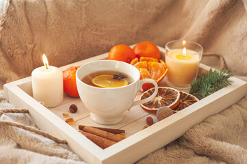 A wooden tray with tea, tangerines, nuts and spices on a beige plaid. Winter breakfast. The concept of hygge.