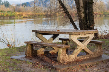 An autumn landscape of the stony table with stony benches in the park by the river. Travel photo, nobody.