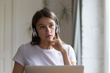 Close up thoughtful woman wearing headphones looking to aside, using laptop, pensive student...