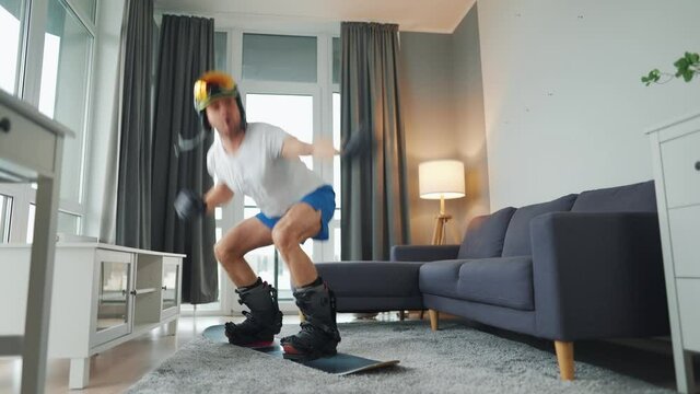 Fun video. Man in shorts and a T-shirt depicts snowboarding on a carpet in a cozy room. Waiting for a snowy winter