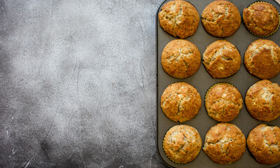 Baked banana and walnut muffins in a muffin pan on a black rogh textured surface