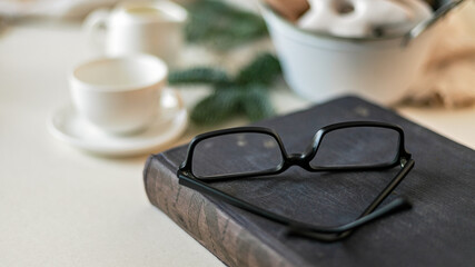 Web banner format. Christmas still life. Old book and glasses in the foreground. White cups and basket with cookies on the background
