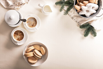 Christmas food flat lay. Gingerbread cookies and macaroons. Aromatic coffee with froth. Gray napkin and fir branches. Beige background.