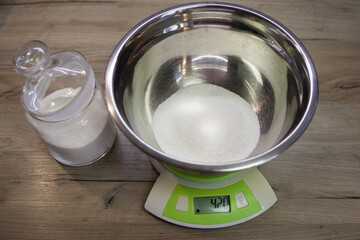 White sugar in a bowl on the scales on the wood background. the first step for making muffins, pie, biscuit. baking process step by step. 420 grams of sugar. weighing products on electronic scales.