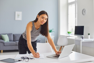 Young woman using laptop and writing in notebook planning her day, working remotely or studying