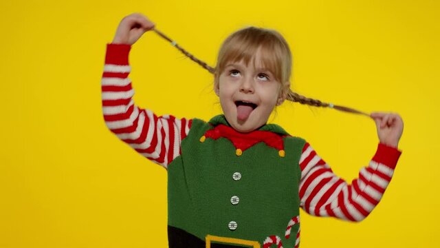 Little fun blonde kid teen teenager girl 5-6 years old in Christmas elf Santa helper costume posing isolated on yellow background. Child dancing, fooling around. People New Year holidays celebration