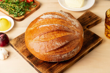 Whole loaf of freshly baked white wheat bread on wooden board on home kitchen table