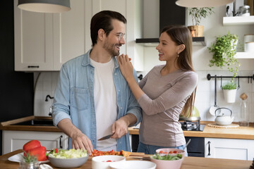Happy young couple hugging, enjoying leisure time in modern kitchen, cooking at home, overjoyed man...