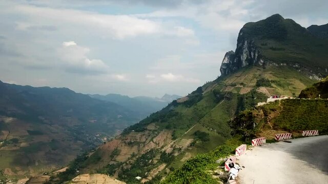 Drone shot of a winding road on the edge of an abrupt mountain at Ma Pi Leng Pass, Vietnam with mountains in the background. Hairpins on the edge of the mountains in South East Asia.