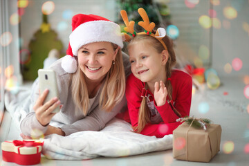 Fototapeta na wymiar Mom and daughter wish Happy New Year by mobile phone for video calls to father, family, friends. Christmas online holiday remote celebration of Christmas in isolation from coronavirus.