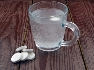 glass with water and effervescent tablets stands on a brown wooden background