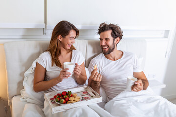 Obraz na płótnie Canvas Couple in love having breakfast in bed. Young caucasian couple having romantic breakfast in bed. Female and male , two cups of coffee, fruits and colorful biscuits.