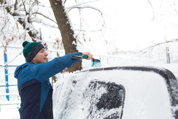 A man brushes snow from a car after a snowfall. A hand in a blue jacket with a car broom on the...
