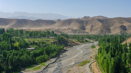 Fototapeta premium Panoramic view of Shahristan river with Zeravshan mountain range in background, at Bunjikat sogdian site. Sughd, Tajikistan