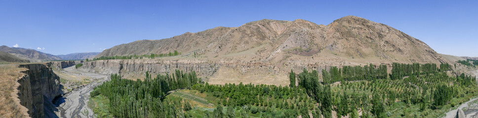 Fototapeta na wymiar Panoramic view of Shahristan river canyon with Zeravshan mountain range in background, near Bunjikat sogdian ruins in Sughd region, Tajikistan