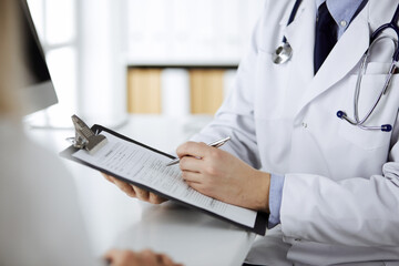 Unknown male doctor and patient woman discussing current health examination while sitting in clinic...