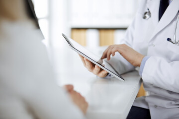 Unknown male doctor and patient woman discussing current health examination while sitting in clinic...
