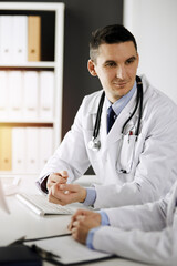 Two doctors colleagues discussing current disease therapy while sitting at working place in sunny clinic. Team work in hospital