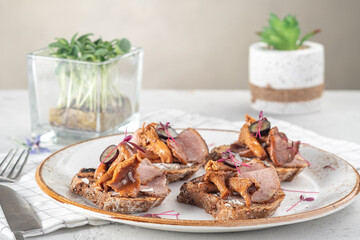 Open sandwiches on rye bread with pickled mushrooms chanterelles and ham on a white plate, close up