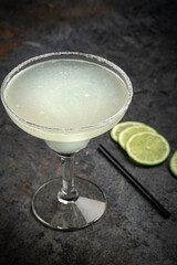 Classic tequila Margarita cocktail in a glass decorated with salt and lime on a stone background, close up