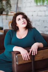 Plus size fashion model in green dress in the interior, fat woman at home