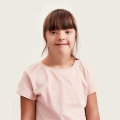 Close up portrait of disabled girl with Down syndrome smiling at camera while posing isolated over...