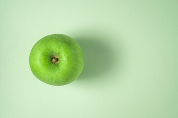 A green apple on a light green background. Flat lay view.