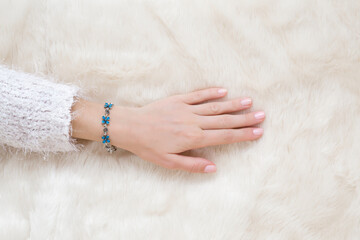 Young adult woman hand touching white fluffy fur blanket. Flower bracelet on female wrist. Closeup. Top down view.