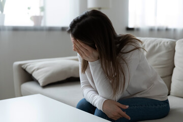 Unhappy frustrated young woman worried about problems, sitting on couch alone, looking to aside, upset sad girl suffering from break up or divorce, feeling depressed, thinking about mistakes