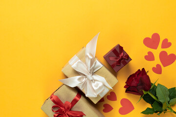 top view on a yellow background lies a red rose near the packed boxes with gifts. Hearts made from cardboard. valentine's day concept