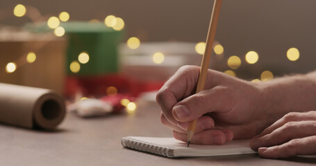 man writes shopping list for holidays in notepad with a pencil under warm light in the evening