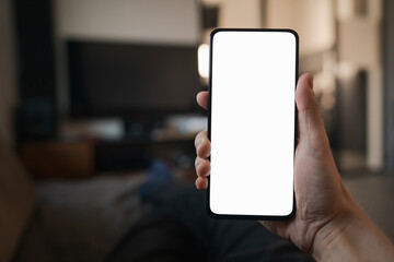 POV photo of man holding smartphone with white screen while sitting on a couch