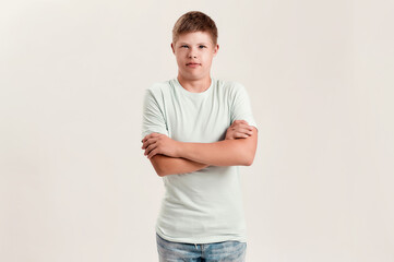 Teenaged disabled boy with Down syndrome looking at camera while posing, standing with arms crossed isolated over white background