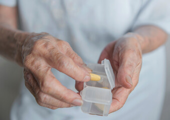 Closeup view of aged senior asian woman taking Pills from white colored transparent plastic medicine box.
Healthcare concept with medicines.
Selective Focus.