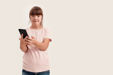 Portrait of disabled girl with Down syndrome looking at camera while using smartphone, standing...