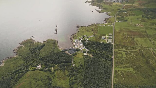 Top down factory at seascape. Aerial nobody nature landscape. Green forest at grass valley. Countryside fields, pastures at sea bay of port town Ellen, Islay Island, United Kingdom, Europe