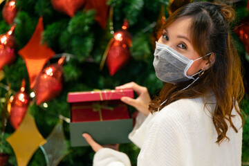 Young woman feels happiness, receive a red box present from family. Opening the box with surprising guess a gift inside in front of Christmas Tree with colorful glitter decoration red and gold at home