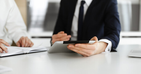 Unknown business people using tablet computer in modern office. Businessman or male entrepreneur is working with his colleague at the desk