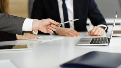 Unknown businessmen and woman sitting, using laptop computer and discussing questions at meeting in modern office, close-up