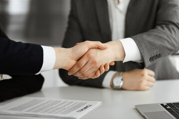 Unknown businessman shaking hands with his colleague or partner above the glass desk in modern office, close-up. Business people group at meeting