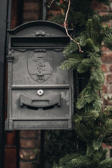Old black vintage mailbox decorated with sprigs of fir for Christmas holidays. Old bricks house.